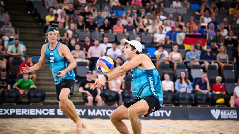 Dynamic beach volleyball action with two players in mid-air near the net.