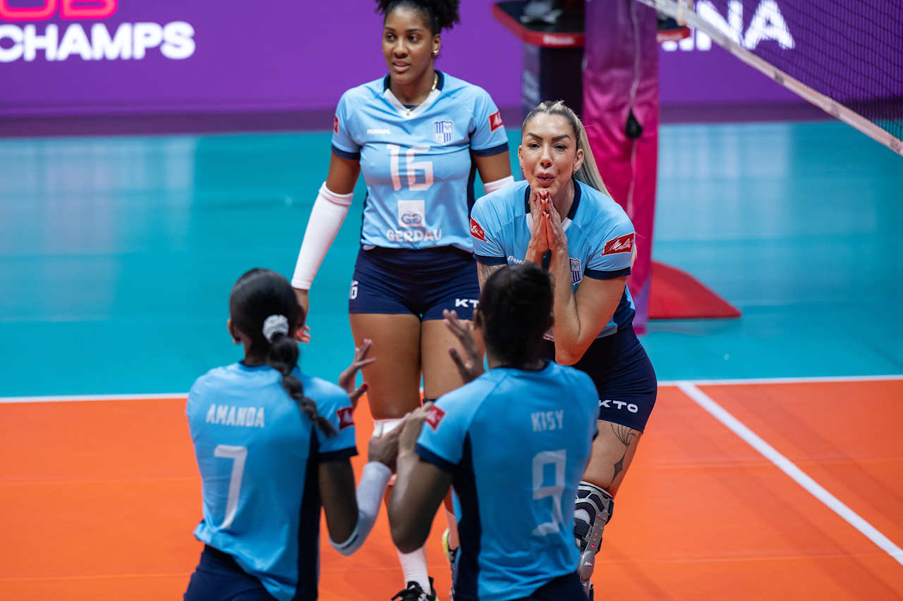 De azul, time do Minas comemora ponto. Thaísa está com as mãos juntos olhando para as companheiras